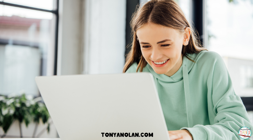 Girl in Green sweatshirt smiling at her laptop screen.